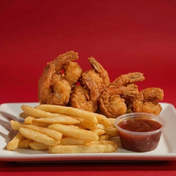 Golden fried shrimp and french fries with a side of dipping sauce on a white plate.